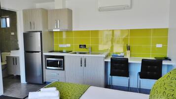 A compact kitchen with a refrigerator, microwave, and sink. There are two black chairs and a small table with a green patterned tablecloth.