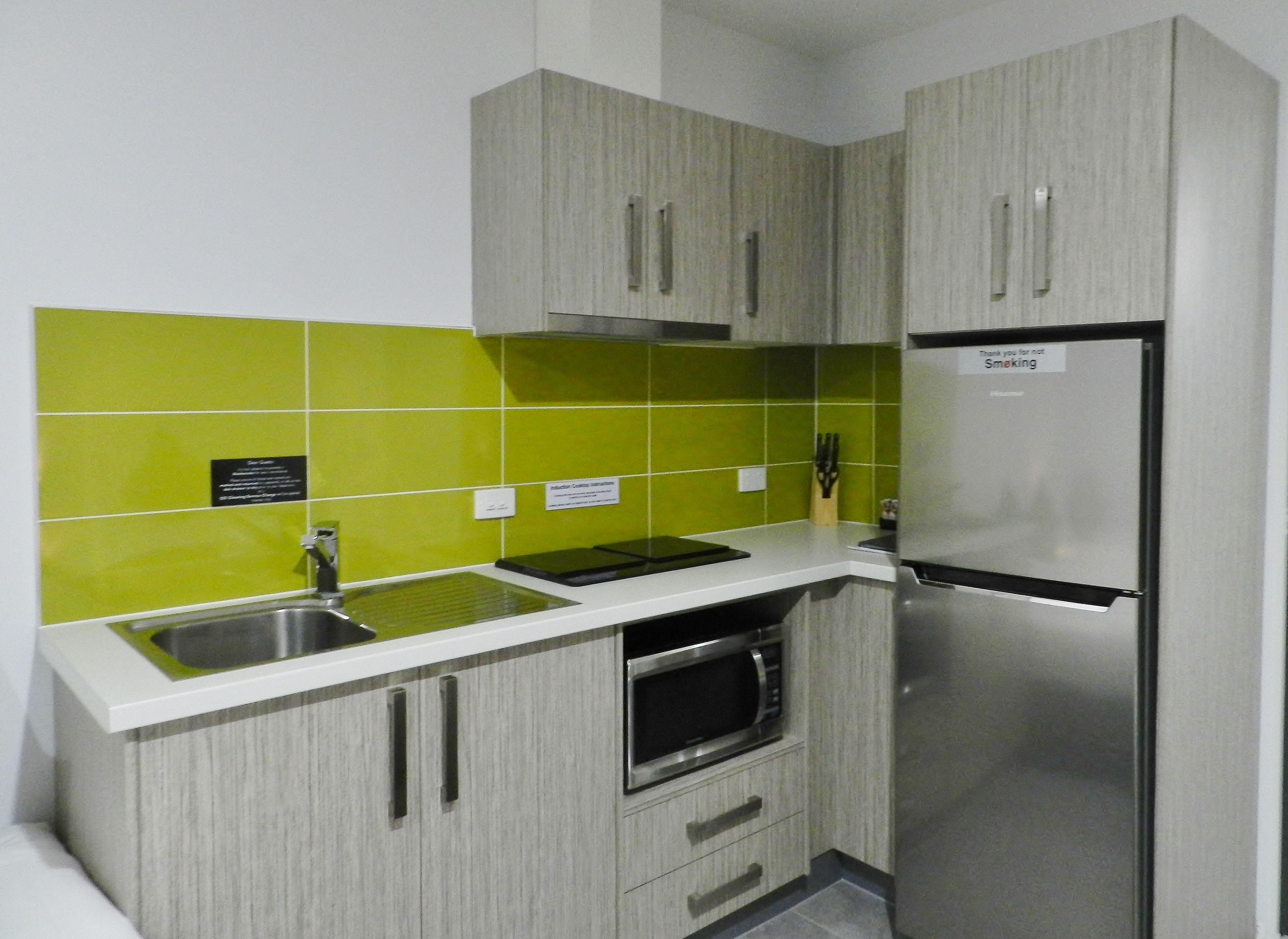 A kitchen with grey cabinets, a stainless steel refrigerator, and a microwave.