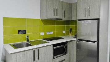 A kitchen with grey cabinets, a stainless steel refrigerator, and a microwave.