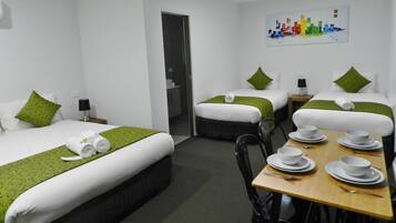A hotel room with two single beds, a dining table with white tableware, and a painting on the wall.