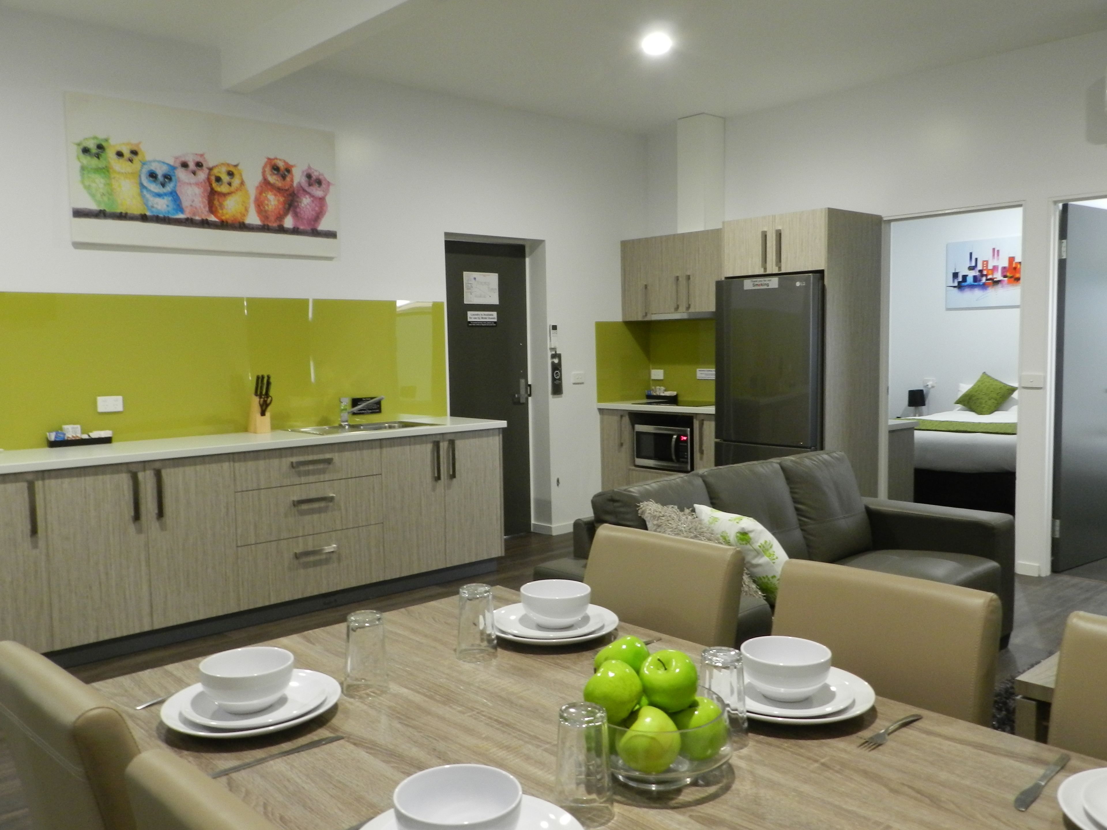 A modern kitchen with a dining area, featuring a table set for four with plates, bowls, and a bowl of green apples.