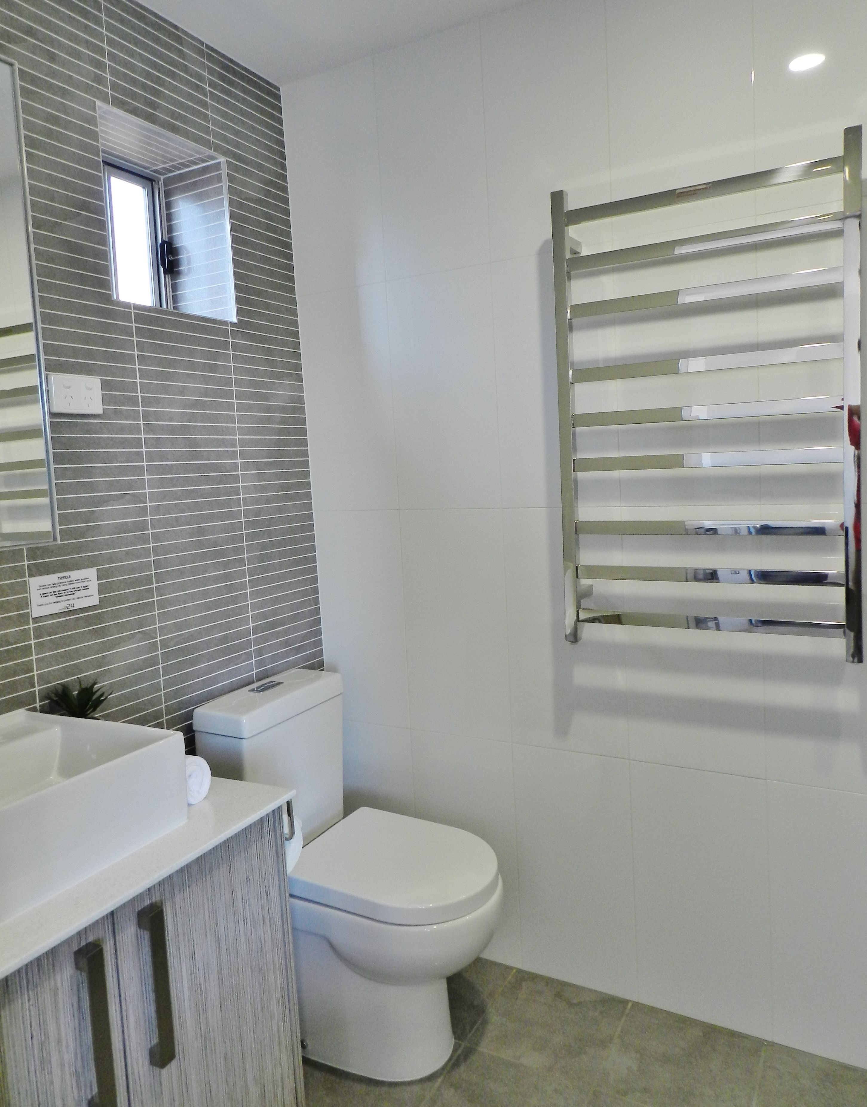 Un baño moderno con inodoro blanco, lavabo con espejo y barra para toallas.