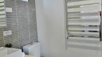 Un baño moderno con inodoro blanco, lavabo con espejo y barra para toallas.
