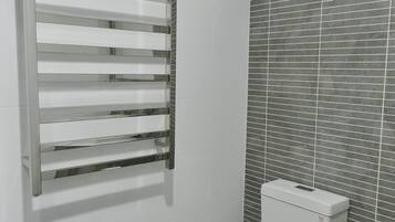 A bathroom with a white toilet, a chrome towel rack, and a tiled wall with a window.