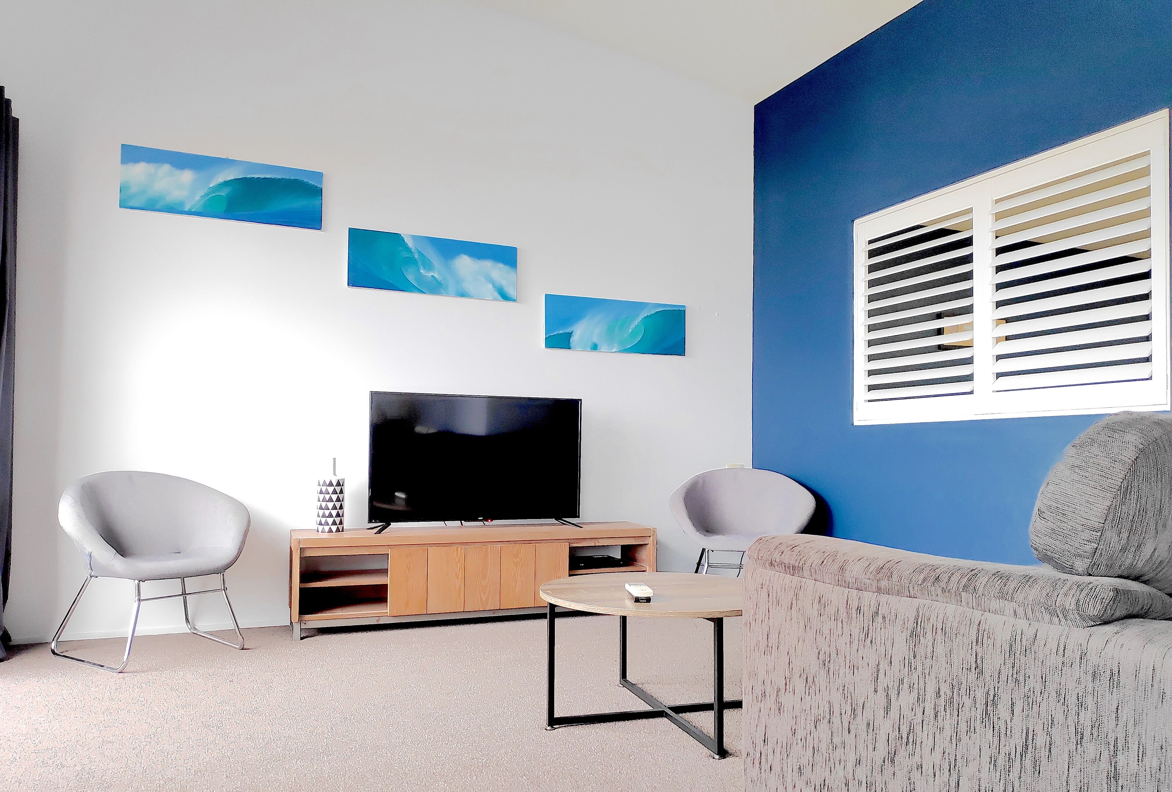 Uma sala de estar moderna com uma televisão de tela plana, duas poltronas cinzas, uma mesa redonda pequena e um móvel de entretenimento de madeira.