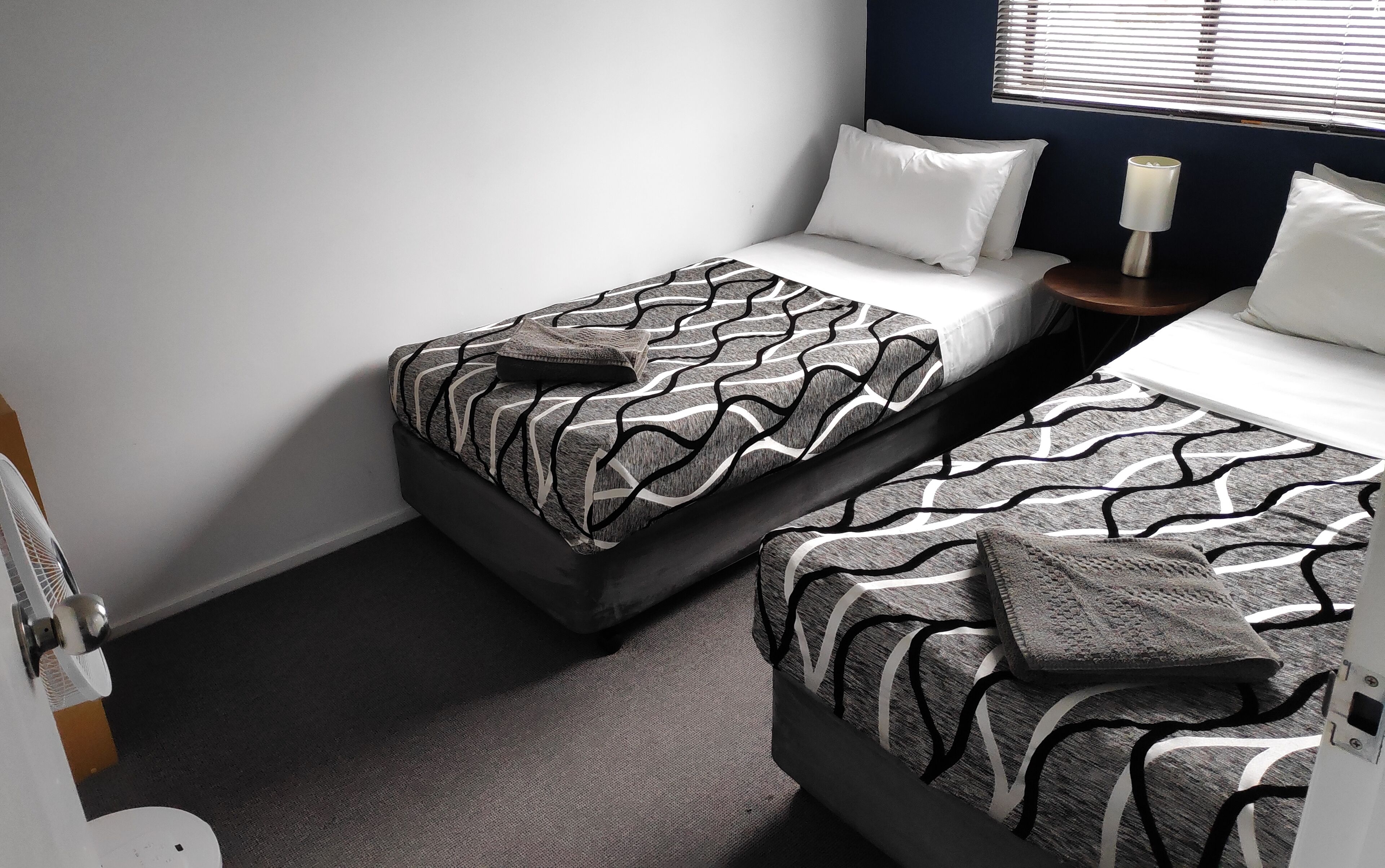 A hotel room with two beds, each with a patterned bedspread, white pillows, and a bedside table with a lamp.
