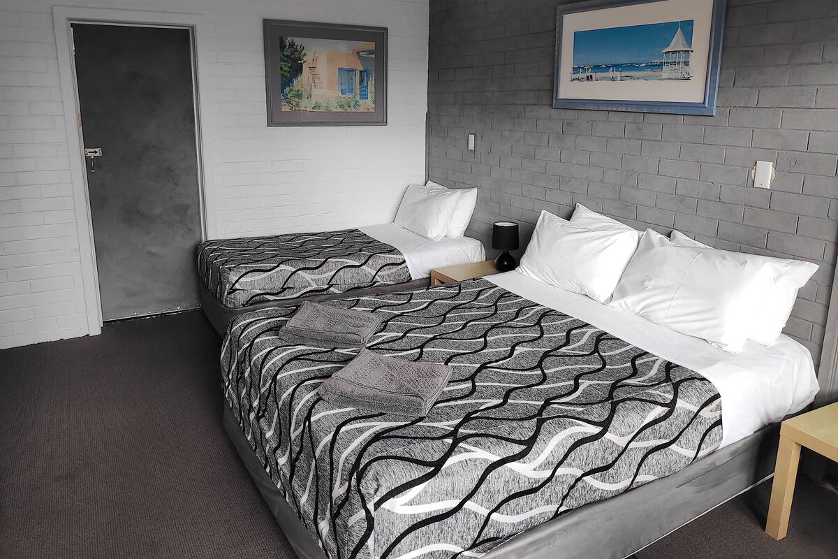 A hotel room with a double bed, two bedside tables, a lamp, and two framed pictures on the wall.