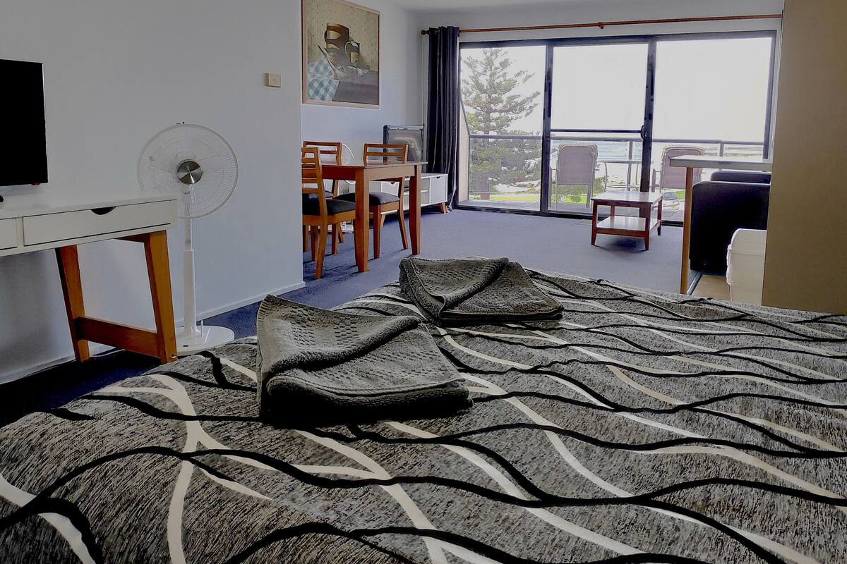 A hotel room with a bed, a desk, a chair, a table, and a large window.