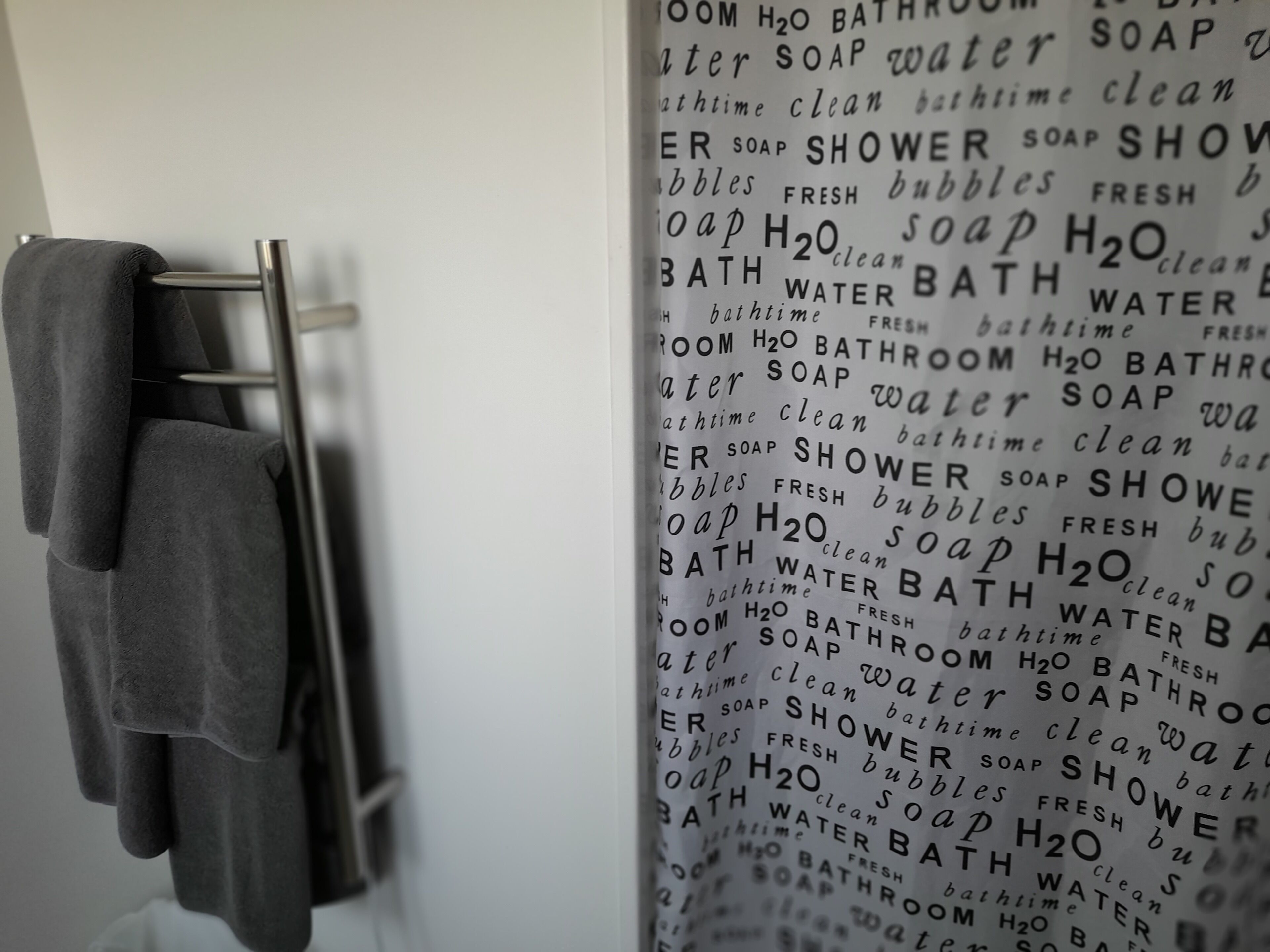 A bathroom with a towel rack holding a dark towel. Text on the wall lists bathroom-related words like 'bathroom,' 'soap,' 'shower,' and 'water.'