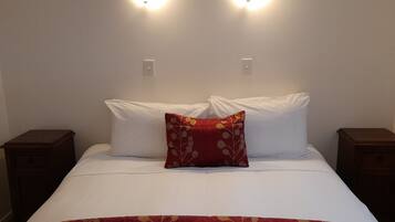 A neatly made bed with white linens and a red floral blanket. There are two bedside tables on either side of the bed, each with a lamp.