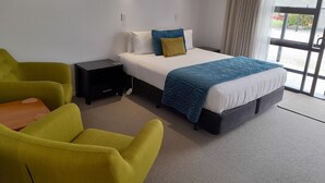 Una camera d'albergo con un letto, un comodino, una scrivania, una sedia e una finestra con tende.