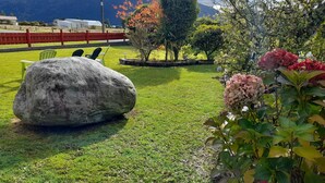 Un'area verde all'aperto con una grande roccia, una recinzione rossa e diversi fiori e piante.