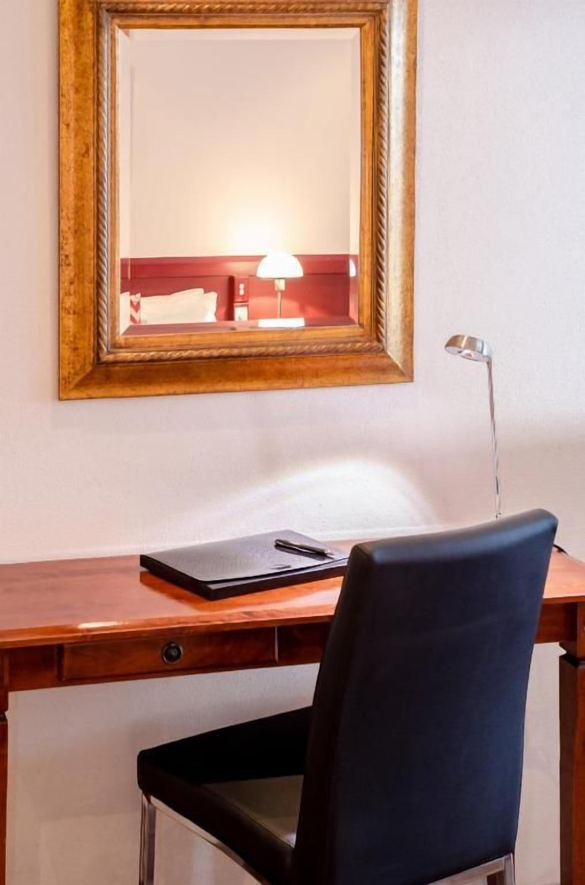 A wooden desk with a black chair, a lamp, and a laptop.