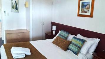 A hotel room with a bed, a nightstand, a wardrobe, a ceiling fan, and two framed pictures on the wall.