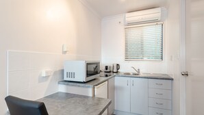 A compact kitchen with a microwave, toaster, and kettle, a small sink, and a window with blinds. - Central Studio Accommodation (Gladstone)