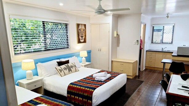 A hotel room with two beds, a desk, a chair, a small kitchenette, and a ceiling fan. - Central Studio Accommodation (Gladstone)