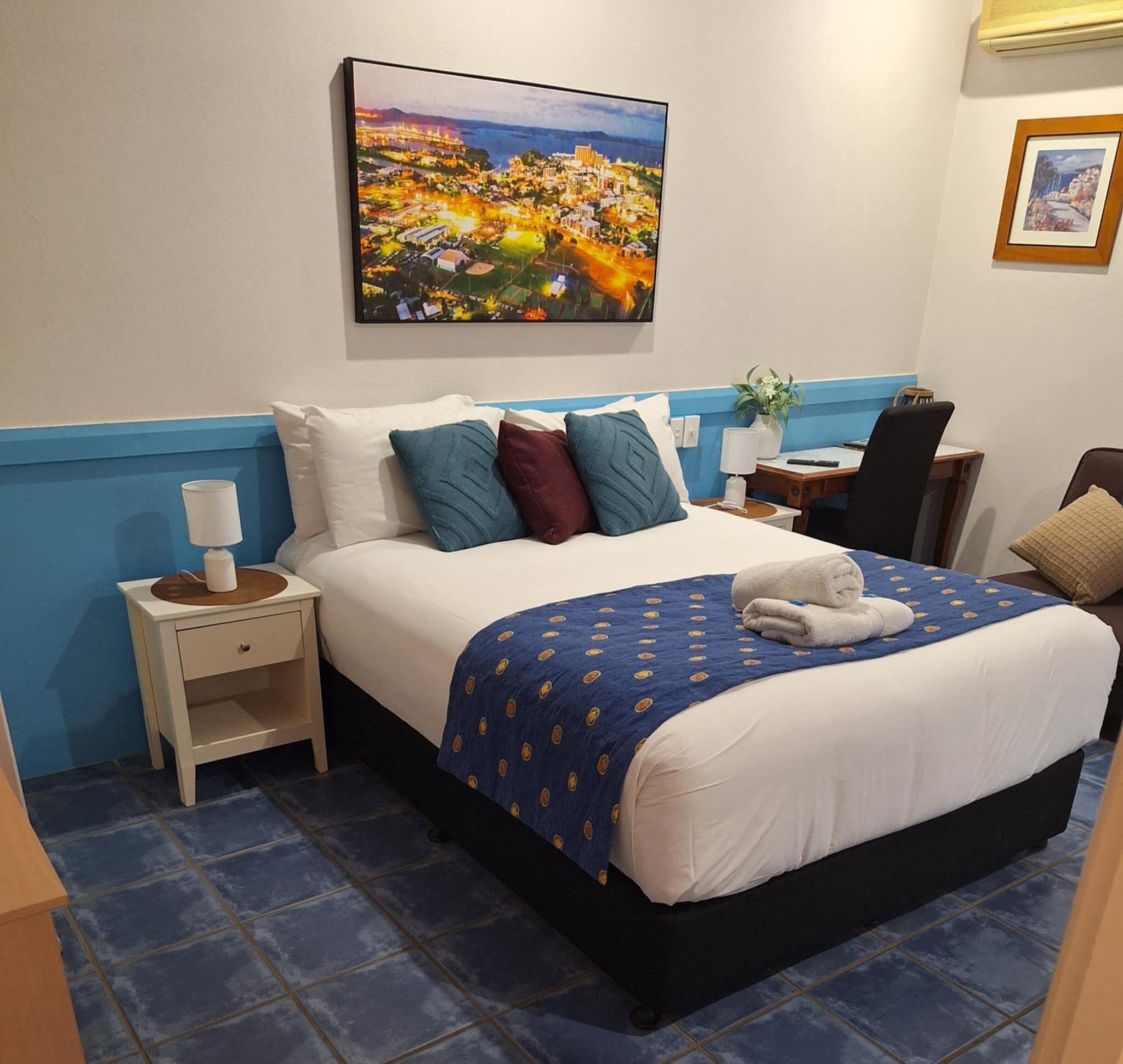 Een hotelkamer met een groot bed, een nachtkastje, een bureau, een stoel en een schilderij aan de muur.