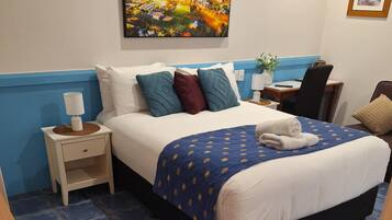 Een hotelkamer met een groot bed, een nachtkastje, een bureau, een stoel en een schilderij aan de muur.