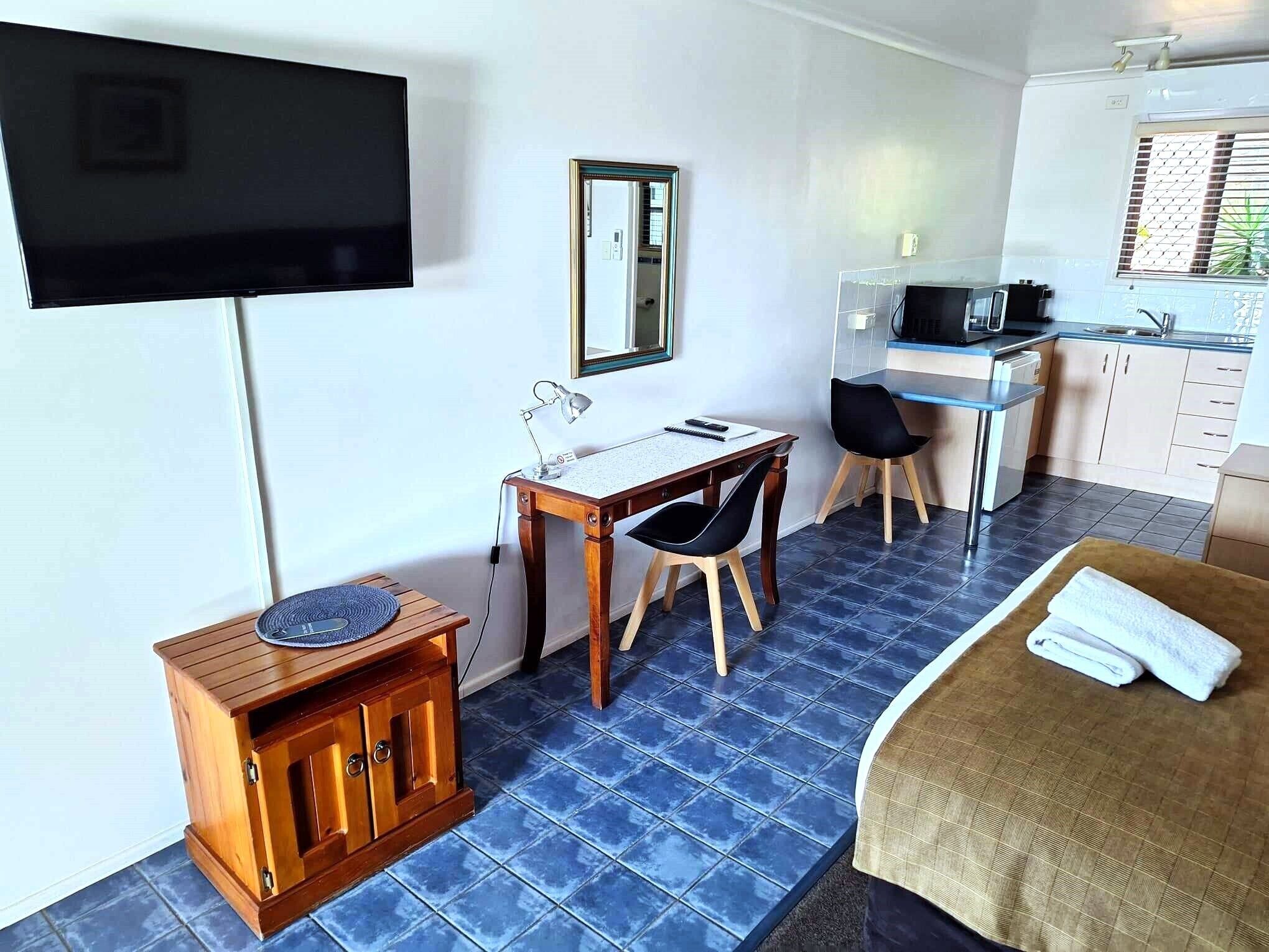 A hotel room with a bed, a desk with a chair, a television, a small cabinet, and a kitchenette.