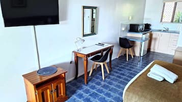 A hotel room with a bed, a desk with a chair, a television, a small cabinet, and a kitchenette.
