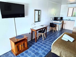 A hotel room with a bed, a desk with a chair, a television, a small cabinet, and a kitchenette. - Central Studio Accommodation (Gladstone)