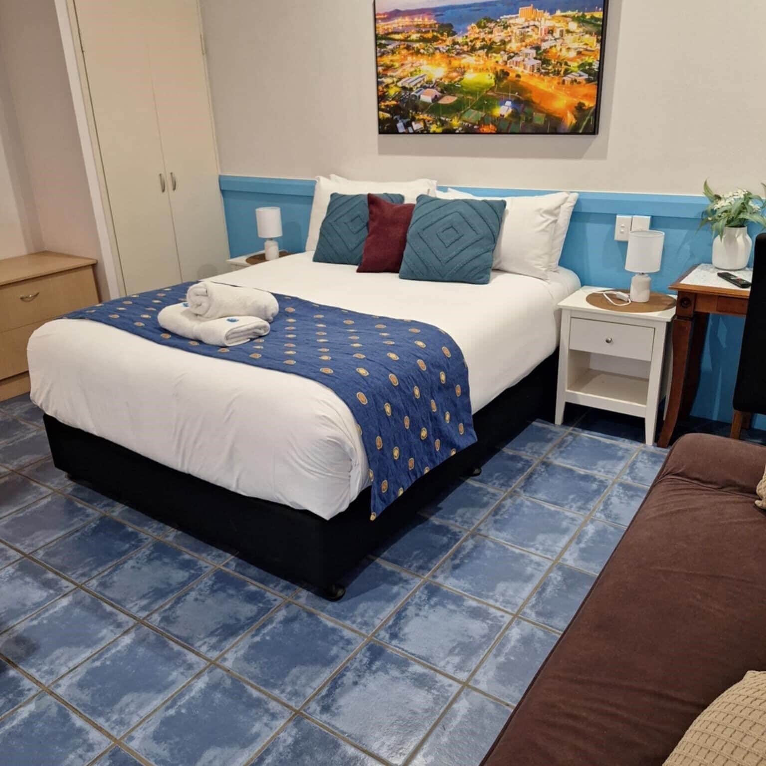 A neatly made bed with a blue and white duvet, a blue and white patterned throw, and a pair of towels.