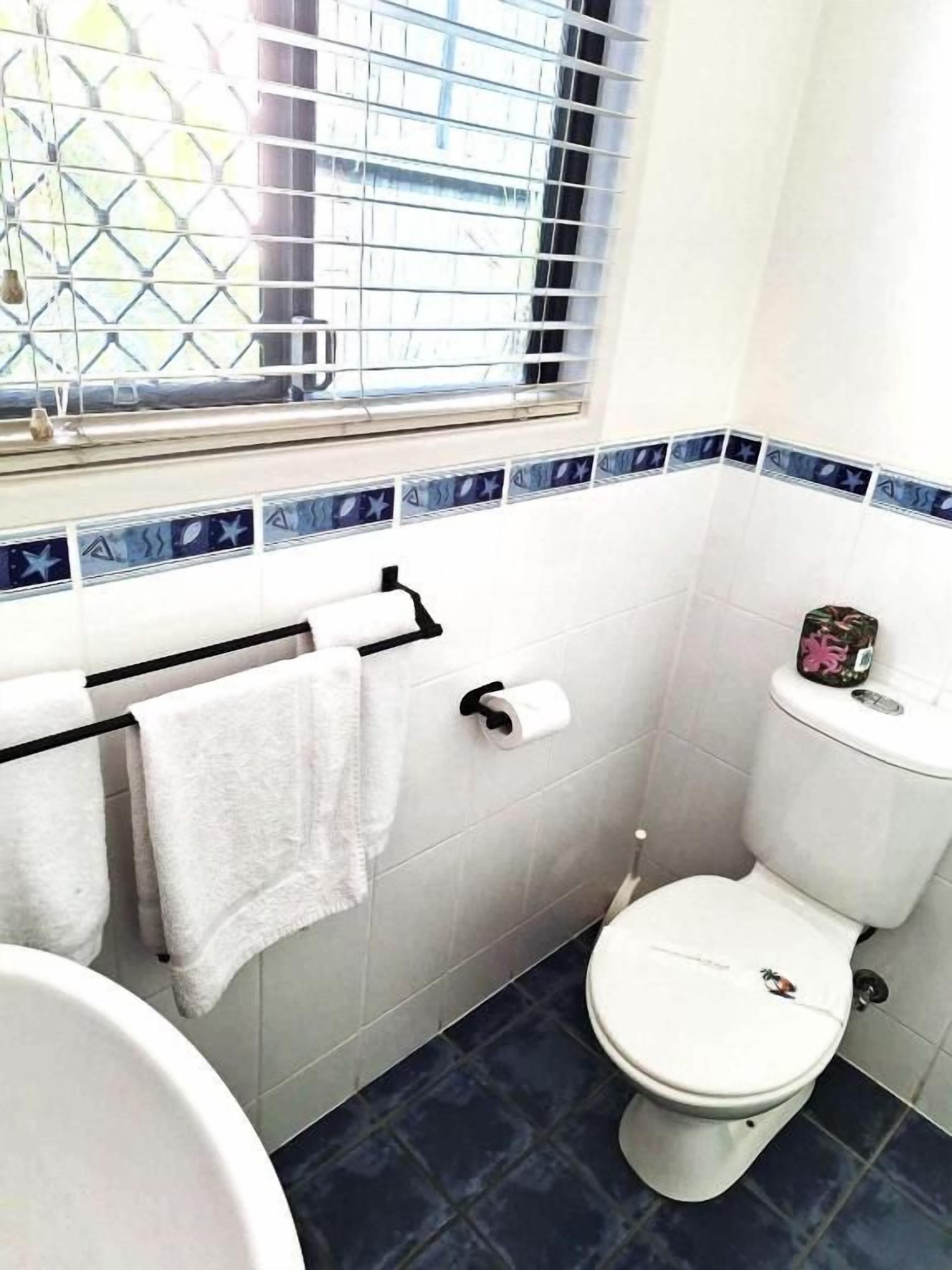 A small bathroom with a toilet, a sink, and a window with blinds.