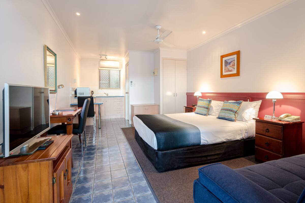 A hotel room with a bed, desk, TV, and a small kitchenette.