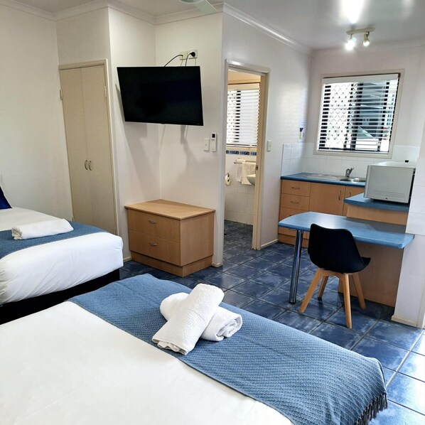 A hotel room with two beds, a desk, a chair, a TV, and a bathroom visible through an open door. - Central Studio Accommodation (Gladstone)