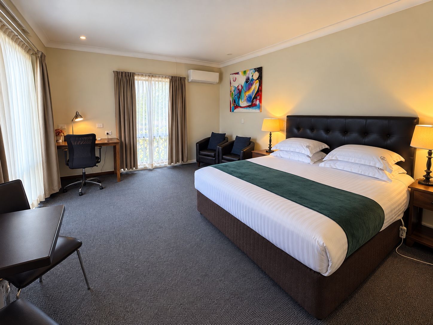 Ein Hotelzimmer mit einem großen Bett, einem Schreibtisch, einem Sessel, einer Schreibtischlampe und einem Bild an der Wand.