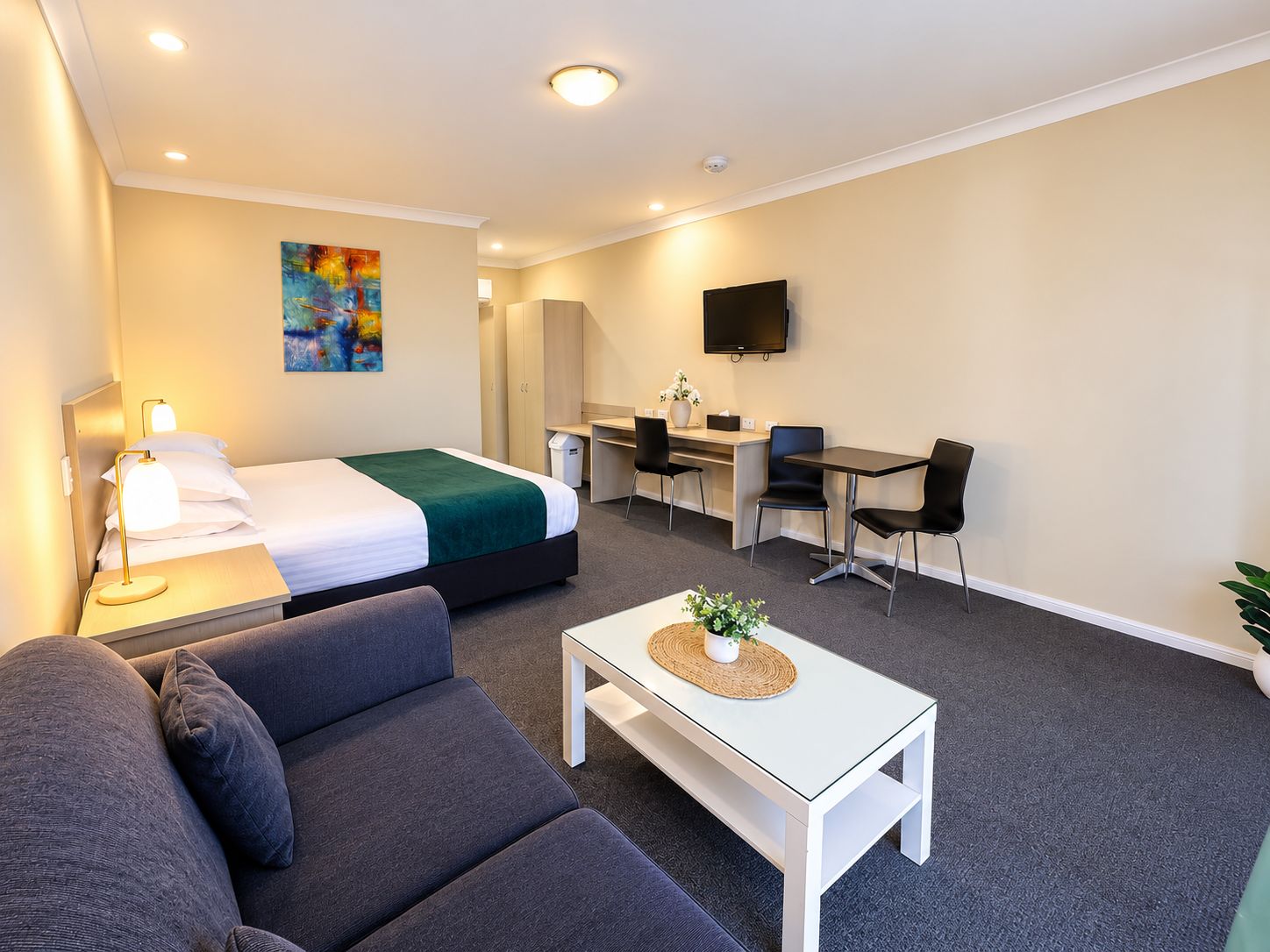A hotel room with a bed, a desk, a TV, a sofa, and a coffee table.