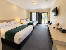 Quarto de hotel com duas camas, uma mesa, uma televisão e uma porta que dá para o exterior.