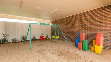 Children can play and build with blocks in this room featuring a swing set and a sandy floor.