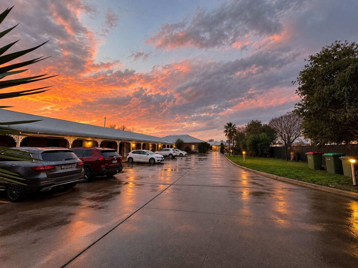 A hotel with a covered parking area, a row of parked cars, and a building with a flat roof.