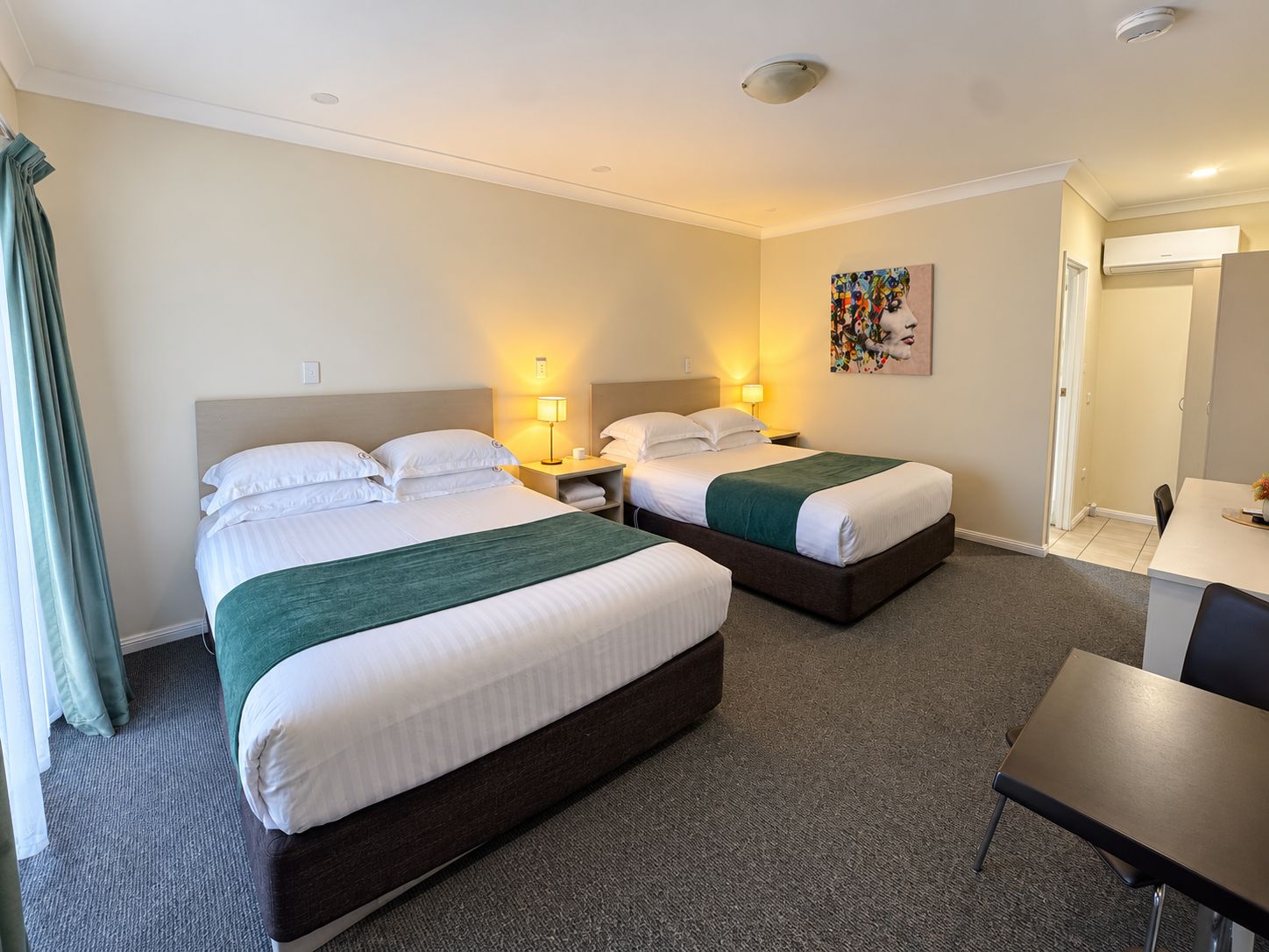 Hotellihuone, jossa on kaksi sänkyä, työpöytä ja tuoli.