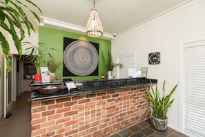 A reception area with a brick counter, green walls, a large circular artwork, a clock, and a potted plant. - Lincoln Cottage Motor Inn (Wagga Wagga)