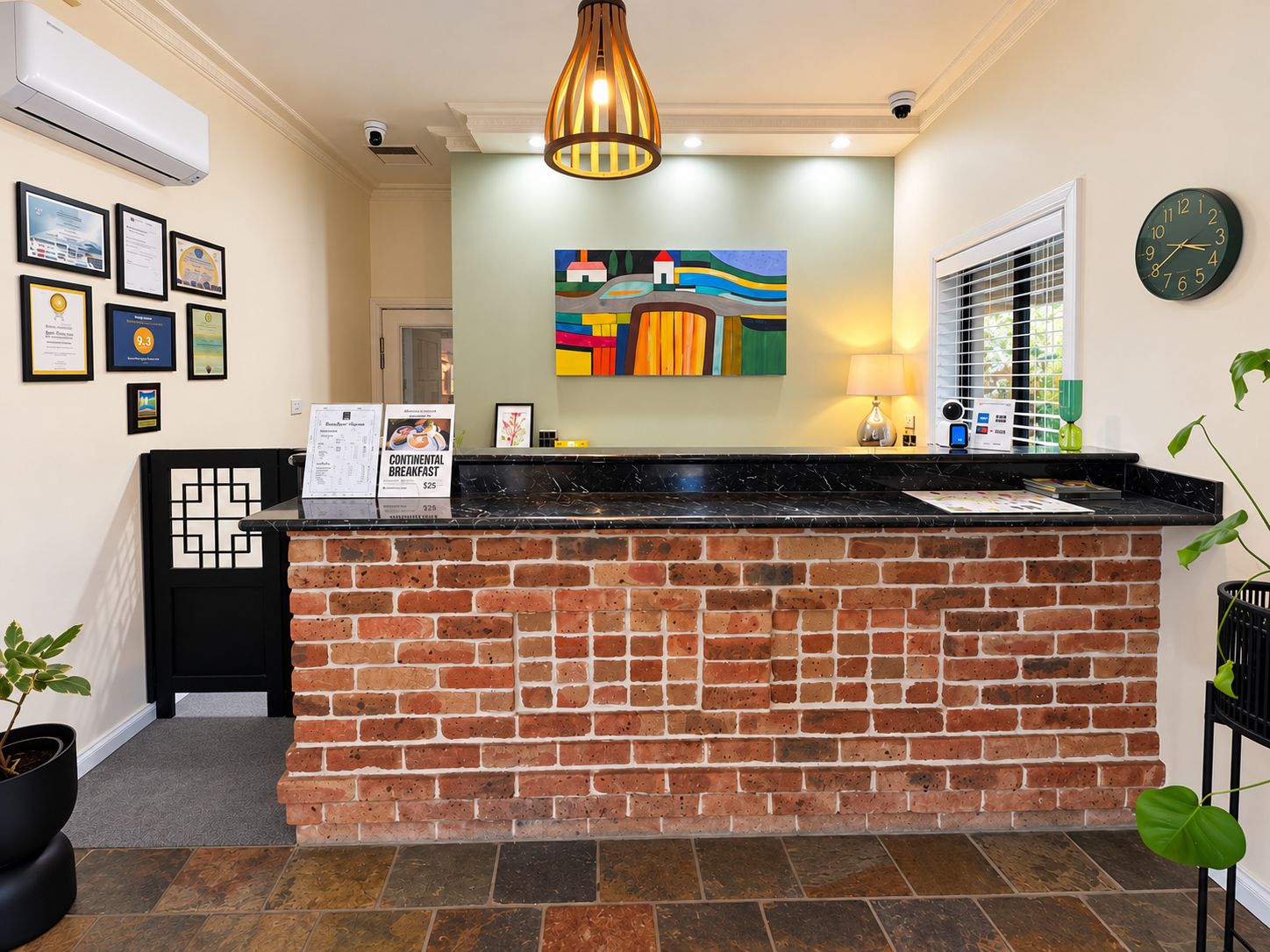 A reception area with a brick counter, framed certificates, a colorful abstract painting, a clock, and a plant.
