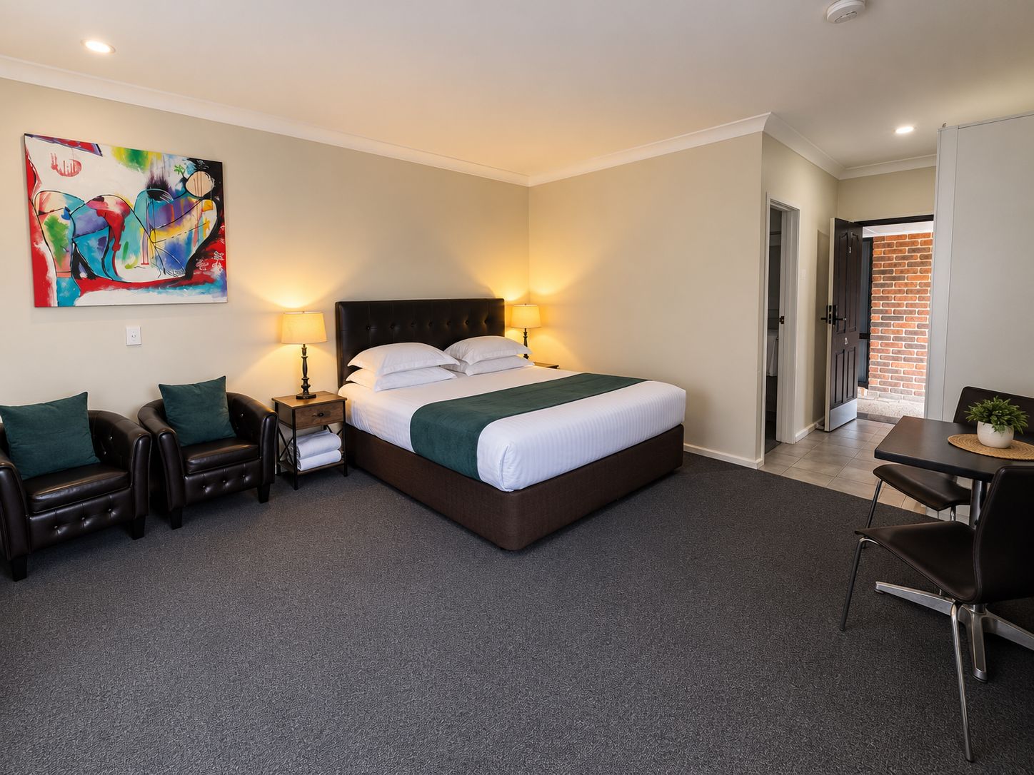 Une chambre d’hôtel avec un lit, deux chaises, un bureau et un tableau au mur.