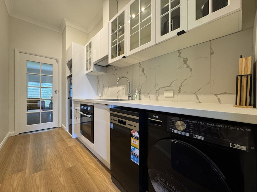 A modern kitchen with white cabinets, a marble backsplash, and a dishwasher.