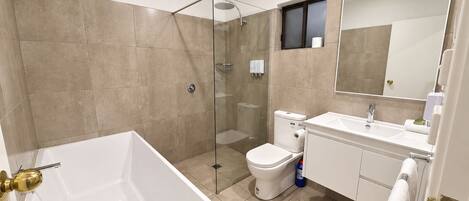 A modern bathroom with a glass-enclosed shower, a white bathtub, and a toilet.