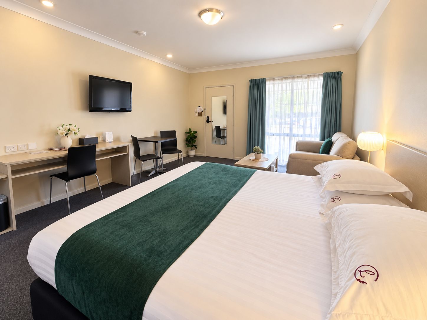 A hotel room with a bed, desk, chairs, a television, and a window with curtains.