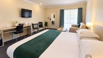 A hotel room with a bed, desk, chairs, a television, and a window with curtains.