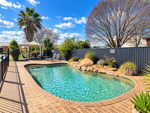 A swimming pool with a curved edge, surrounded by a brick deck and a metal fence. - Lincoln Cottage Motor Inn (Wagga Wagga)