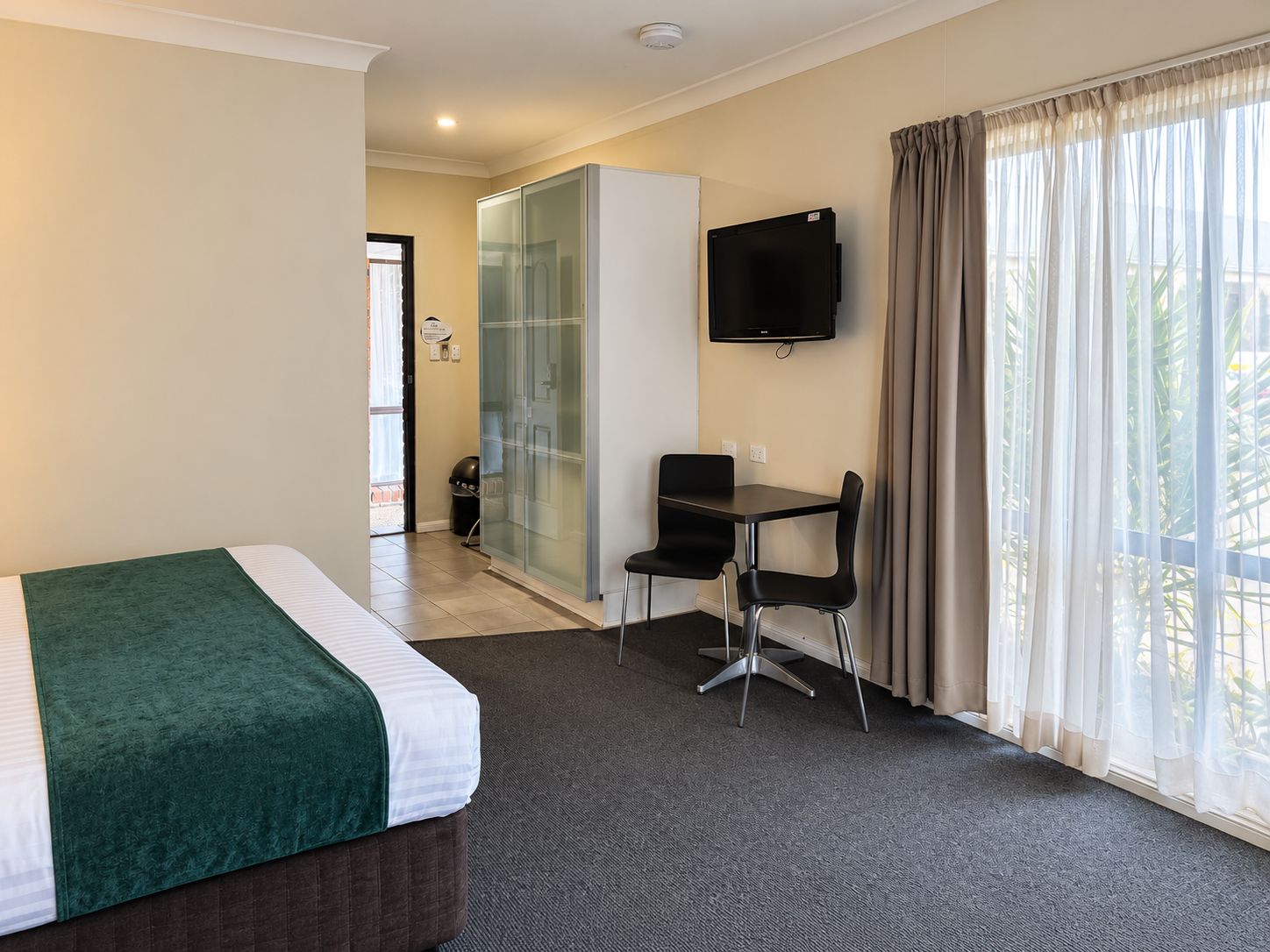 Une chambre d’hôtel avec un lit, un bureau, une chaise, une télévision et une fenêtre avec des rideaux.