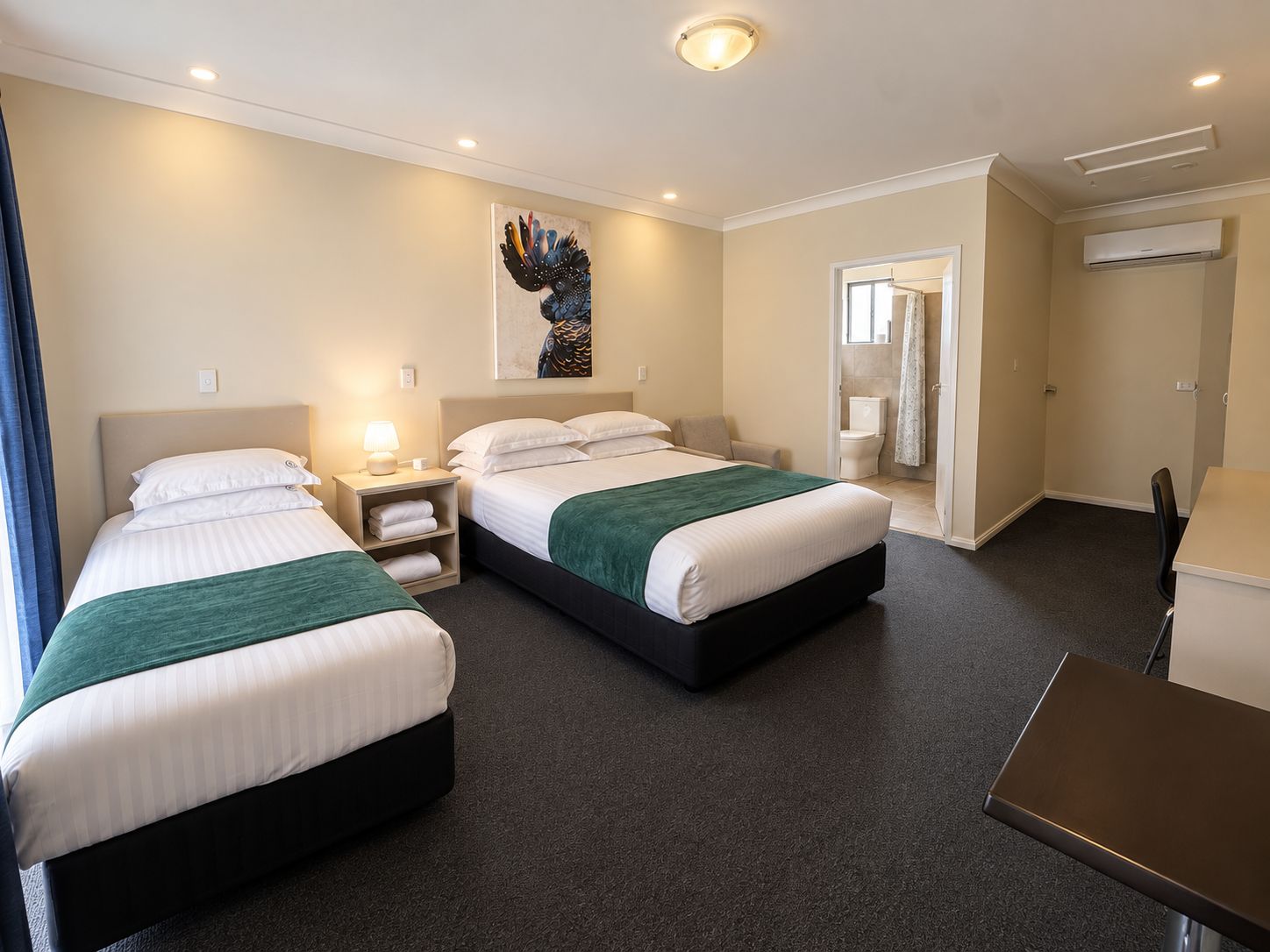 Een hotelkamer met twee bedden, een bureau en een zichtbare badkamer door een geopende deur.