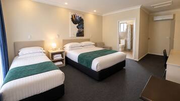 Een hotelkamer met twee bedden, een bureau en een zichtbare badkamer door een geopende deur.