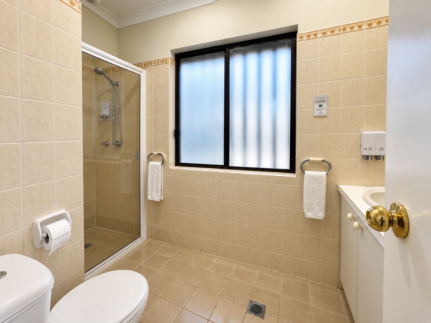 A bathroom with a toilet, shower, and window.