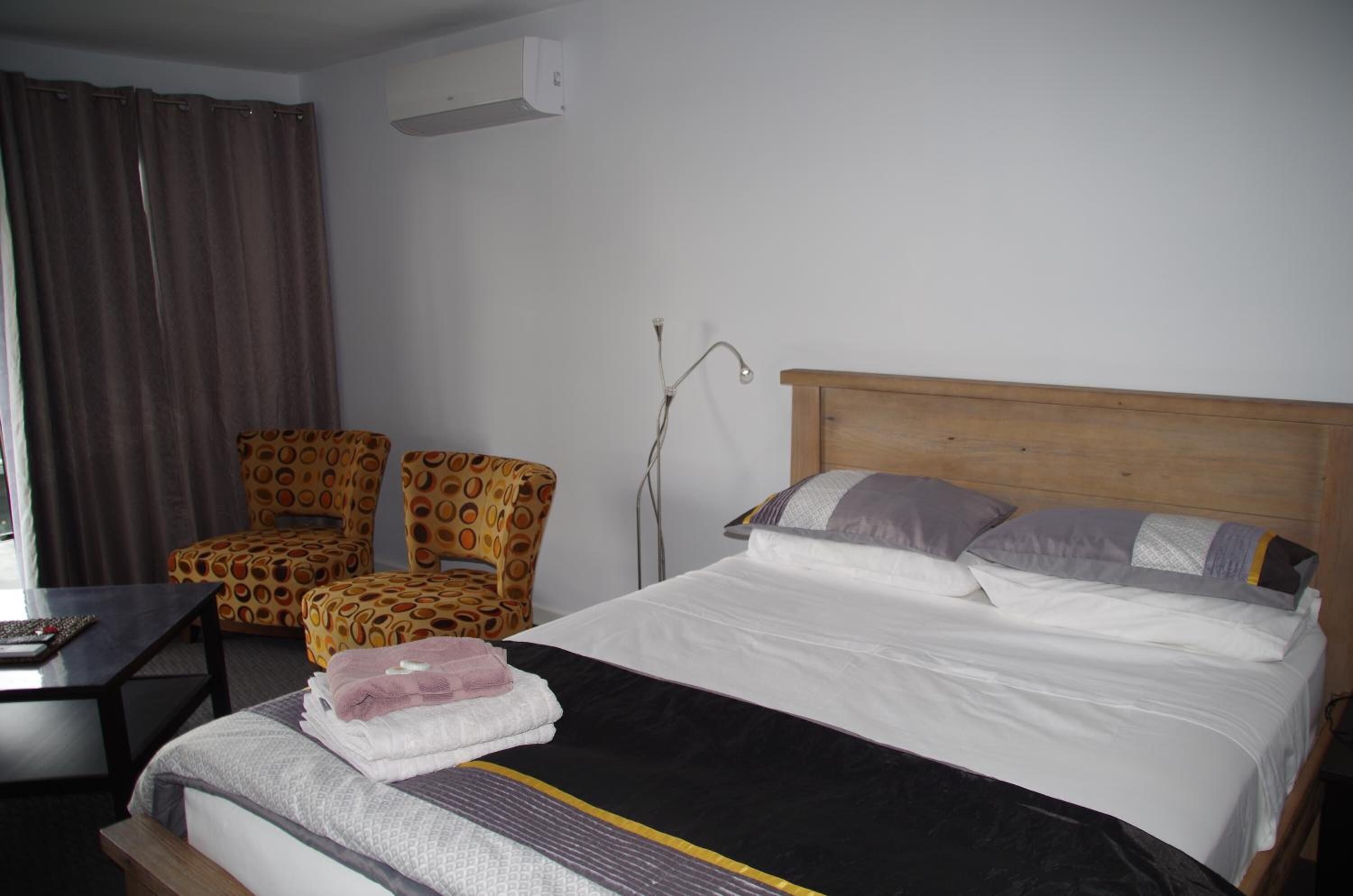 A hotel room with a bed, two patterned chairs, a small table, and a bedside lamp.