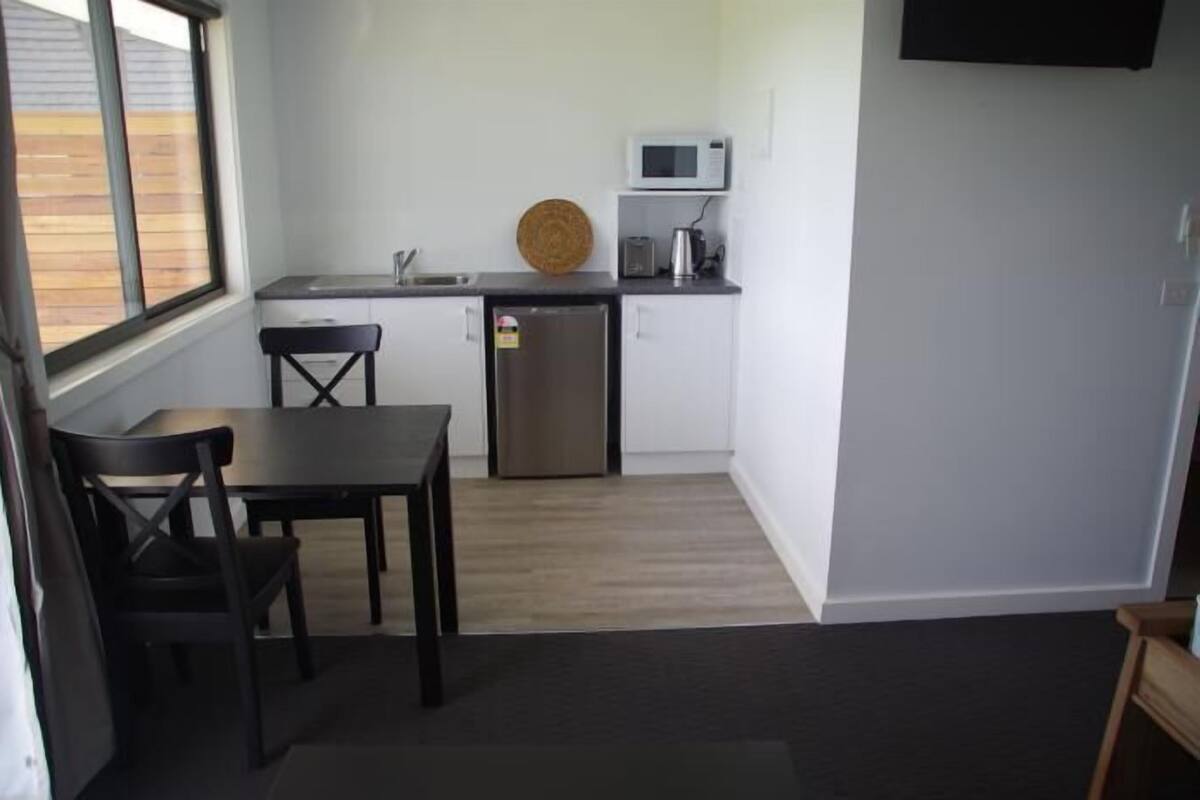 Cocina compacta con microondas, tostadora y refrigerador. Hay una mesa de comedor con sillas y una ventana que proporciona luz natural.
