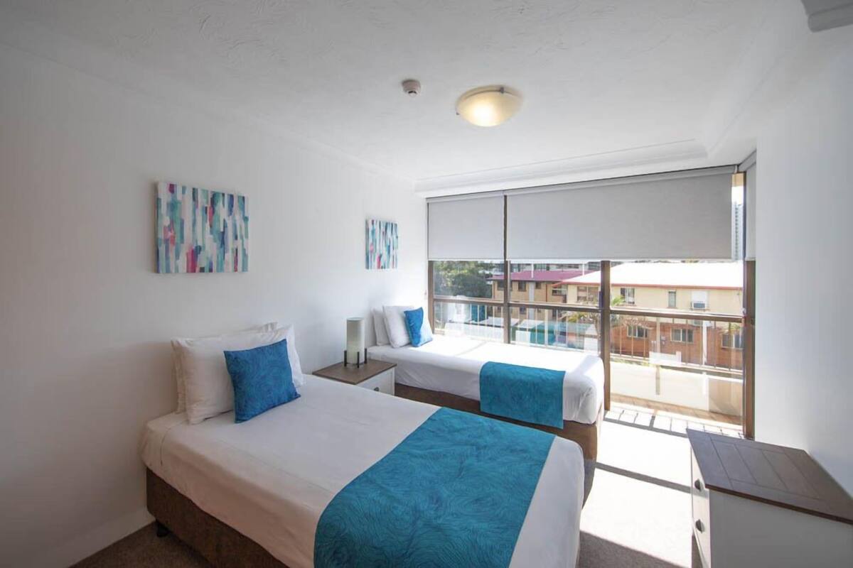 A hotel room with two beds, a large window, and artwork on the walls.
